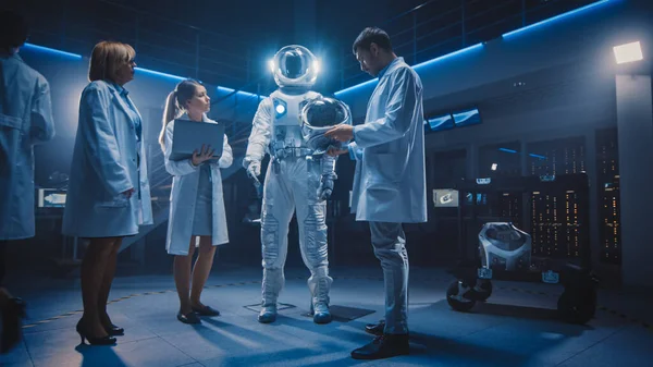 Team of Aerospace Forskare och ingenjörer bär vita rockar har diskussion, använda datorer, Konstruera Astronaut hjälm för New Space Suit Anpassad för utforskning och resor. Lågvinkelskott — Stockfoto