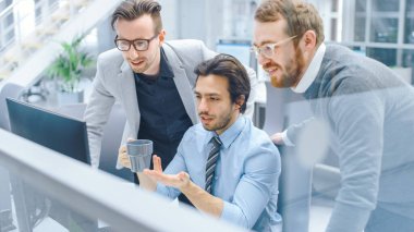 Parlak Modern Ofis: Ofis İşçisi Masaüstü Bilgisayarında Oturup Çalışırken, Proje Müdürü ve Takım Lideri ile Sorun Çözümünü Tartışıyor. Genç İş Adamları Planlama ve Problem Çözme