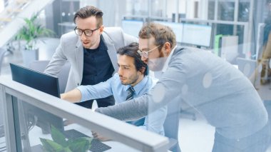 Parlak Modern Ofis 'te: İşadamı Masaüstü Bilgisayarında Oturuyor ve Çalışıyor, Proje Yöneticisi ve Takım Lideri Onun Yanında Duruyor. Tartışıyorlar, Problem Çözümünü Buluyorlar, Ekranı Gösteriyorlar