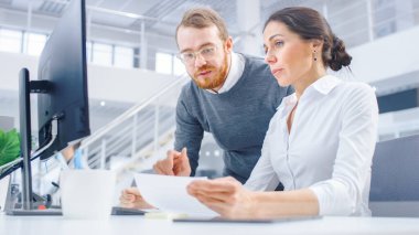 Parlak Modern Ofiste: Güzel İşkadını Masaüstü Bilgisayarında, Proje Yöneticisi Yanında Dururken Oturup Çalışıyor, Tartışıyorlar, Sorun Çözümünü Buluyorlar 