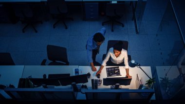 Ofiste Gece Geç Saatlere Kadar Çalışmak: İş kadını ve İşadamı Masaüstü Bilgisayarı Kullanıyor, Tartışıyor, Analiz ediyor, Belgeleri Kullanıyor, Sorunları Çözüyor, Projeyi Bitiyor. Yüksek Açı Atışı