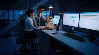 Modern Ofiste Gece Geç Saatler: İşadamı ve İş kadını Masaüstü Bilgisayarı Üzerinde Çalışıyor, Tartışıyor, Problem Çözümü Buluyor, Projeyi Bitiyor. Başarılı Sorumluluk Sahipleri Bürosu çalışanları