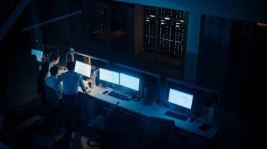 Modern Ofiste Gece Geç Saatler: Başarılı İş Adamları ve İş Kadınlarından oluşan Çeşitli Ekip Bilgisayar Etrafında Toplanıyor, Tartışıyor, Problem Çözümünü Buluyor, Projeyi Birlikte Tamamlıyor. Yüksek Açı