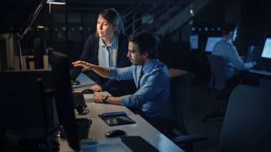 Hırslı İşadamı Masaüstü Bilgisayarını Kullanıyor, Onun Kadın Proje Yöneticisi Özel Görevleri, Hesaplama ve Stratejik Hareketleri Açıklıyor. Büyük Şirket Ofisinde Profesyonel İnsanlar Geceleyin Geç Saatlere Kadar Çalışıyor