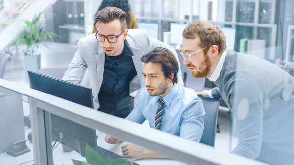 In Bright Modern Office: Young Businessman sitting and Working at His Desktop Computer with Project Manager and Team Leader Standing Beside Him, Have Discussion, Finding Problem Solution — 스톡 사진