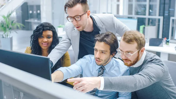 Dans le bureau moderne : équipe diversifiée d'hommes d'affaires et de femmes d'affaires travaillent sur ordinateur, discutent, essaient de trouver une solution aux problèmes collectivement. Les jeunes gens d'affaires parlent et pointent du doigt à l'écran — Photo