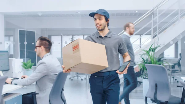 Happy Delivery Man entra en la oficina corporativa y entrega el paquete de cartón a un trabajador. Oficina moderna brillante grande de la compañía del negocio con los empresarios profesionales que trabajan — Foto de Stock