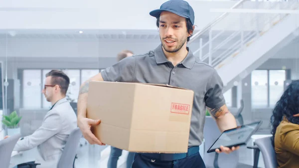 Happy Delivery Man Wals en la oficina corporativa con Tablet Computer y entrega el paquete de cartón a un trabajador. Oficina moderna brillante grande de la compañía del negocio con los empresarios profesionales que trabajan — Foto de Stock