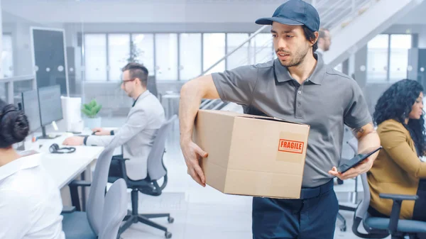 Happy Delivery Man marche dans le bureau d'entreprise avec tablette et livre le paquet de carton à un travailleur. Bureau d'entreprise moderne lumineux Big Bright avec des hommes d'affaires professionnels travaillant — Photo