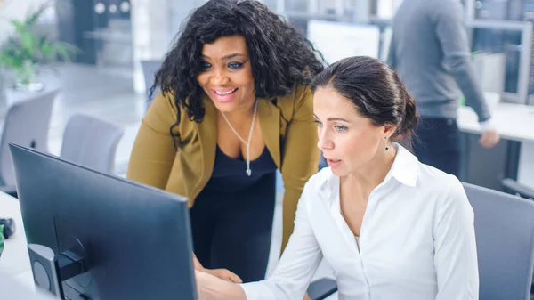 In Bright Modern Office: Beautiful Businesswoman sitting and Working at Her Desktop Computer with Female Project Manager Standing Beside Her, They Have Discussion, Find Problem Solution — 스톡 사진