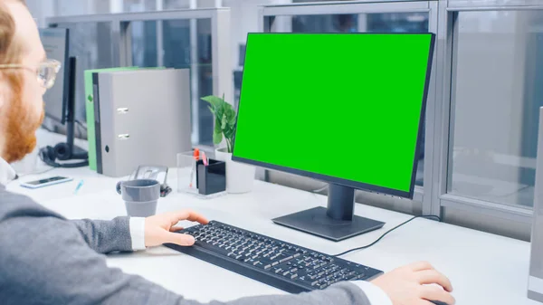 Sobre o tiroteio do ombro do trabalhador de escritório motivado usando o computador de mesa verde da tela do Mock-up no escritório aberto brilhante grande do espaço — Fotografia de Stock