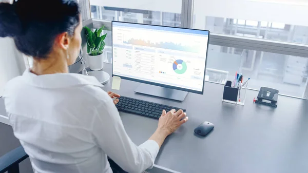 Im Großraumbüro arbeitet eine Geschäftsfrau an ihrem Personal Computer mit Finanzdaten, Grafiken und Statistiken. Gedreht im großen hellen modernen Großraumbüro. — Stockfoto