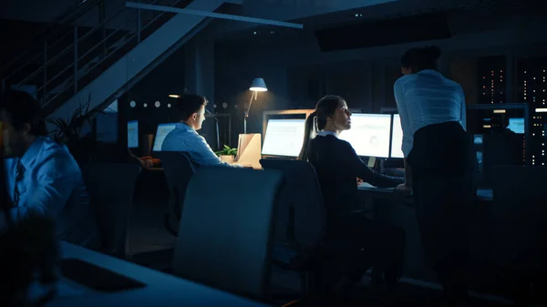 Sent på natten i det moderna kontoret: Olika team av framgångsrika affärsmän och affärskvinnor arbetar på stationära datorer, ha diskussioner, hitta problemlösningar, slutföra projektet — Stockfoto