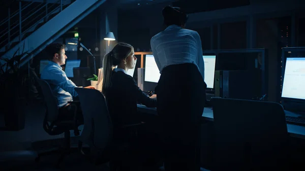 Tard dans la nuit dans le bureau moderne : équipe diversifiée d'hommes d'affaires et de femmes d'affaires prospères travaillent sur des ordinateurs de bureau, discutent, trouvent des solutions aux problèmes, finissent le projet — Photo