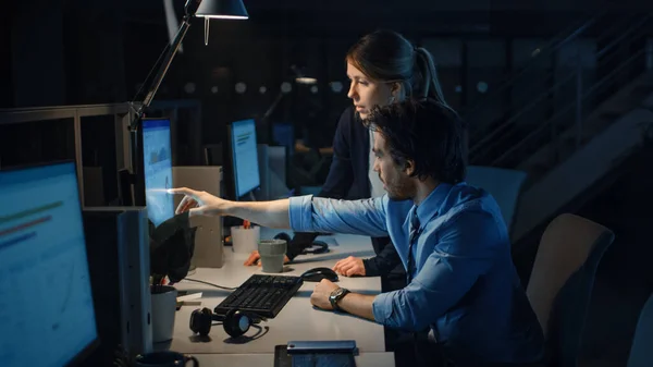 Empresario ambicioso utiliza computadora de escritorio, su gerente de proyecto femenino explica tareas específicas, manejo de cuentas y movimientos estratégicos. Gente profesional tarde en la noche en la oficina corporativa grande —  Fotos de Stock