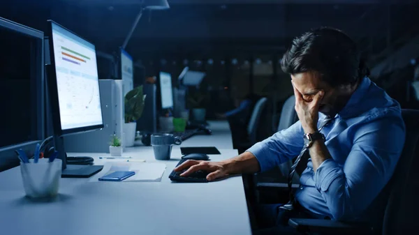 No escritório à noite sobrecarregado cansou o trabalhador do escritório usa computador desktop e cobre seu rosto com sua mão. Cansado Empresário Exausto Acabamento Projeto Importante — Fotografia de Stock