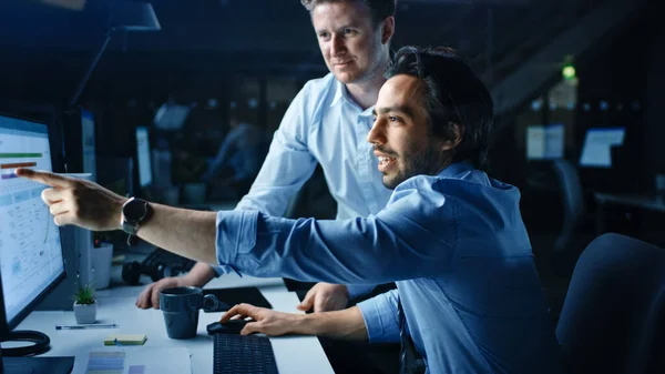 Empresario ambicioso y confiado utiliza computadora de escritorio, su gerente de proyecto explica tareas específicas, manejo de cuentas y movimientos estratégicos. Gente profesional tarde en la noche en la oficina corporativa grande — Foto de Stock