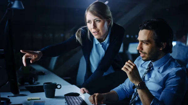 Selbstbewusster Geschäftsmann verwendet Desktop-Computer, seine Managerin erklärt spezifische Aufgaben, Kontoführung und Strategie. Berufstätige debattieren und streiten spät in der Nacht im Büro. — Stockfoto