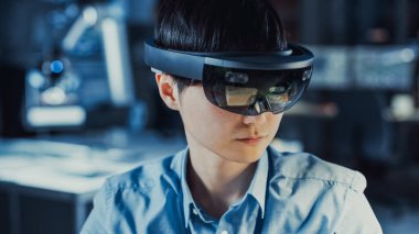 Profesyonel Japon Elektronik Geliştirme Mühendisi Mavi Gömlekli Sanal Gerçeklik Kulaklığı takıyor ve Modern Bilgisayar Ekipmanları ile Yüksek Teknoloji Araştırma Laboratuvarına Bakıyor.