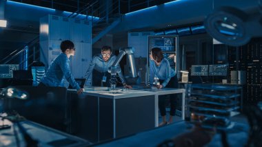 Fütürist Robotik Kol Metal Nesneyi Hareket ettiriyor ve Yerleştiriyor. Kıdemli Mühendis, bu Gelişmiş Süreci Çeşitli Ekibiyle Görüşüyor. Modern bir yüksek teknoloji araştırma laboratuvarındalar.