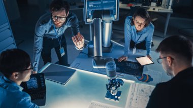 Fütürist Robotik Kol Metal Nesneyi Kaldırıyor ve Taşıyor. Kıdemli mühendis bu gelişmiş süreçte konuşuyor. Modern ekipmanlarla Yüksek Teknoloji Araştırma Laboratuvarındalar. Yukarıdan çekilen.