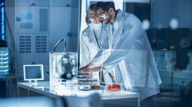 Çeşitli Uluslararası Endüstriyel Bilimadamları ve Mühendisler Takımı, Araştırma Laboratuvarında Ağır Makineler Tasarımı üzerinde çalışan beyaz önlük giyiyorlar. 3D Yazıcı, Bilgisayar ve Mikroskop kullanan Profesyoneller