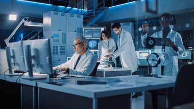Endüstriyel Bilimadamları ve Mühendislerden oluşan çeşitli uluslararası bir ekip, Araştırma Laboratuvarında Endüstriyel Makine Tasarımı üzerinde çalışan beyaz önlük giyiyor. Bilgisayarları ve Konuşmayı Kullanan Profesyoneller