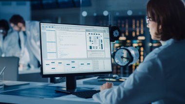 Omuz Fotoğrafı Üzerinde: Kadın Bilişim Bilimcisi Bilgisayar Gösterme Sistemi İzleme ve Kontrol Programı Kullanıyor. Bilim adamları ve Mühendislerle Arka plan Teknoloji Geliştirme Laboratuvarında