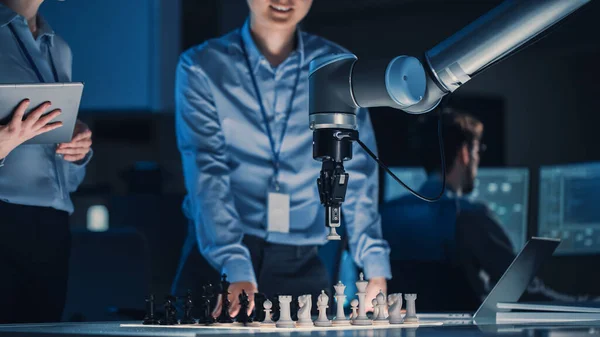 Dos ingenieros de desarrollo están discutiendo y probando una interfaz de inteligencia artificial jugando ajedrez con un brazo robótico futurista. Están en un Laboratorio de Investigación Moderna de Alta Tecnología. — Foto de Stock