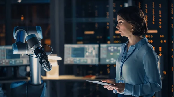 Ingeniera femenina con Tablet Computer Analiza cómo funciona un brazo robótico futurista y mueve un objeto metálico. Laboratorio de investigación de alta tecnología con equipos modernos. — Foto de Stock