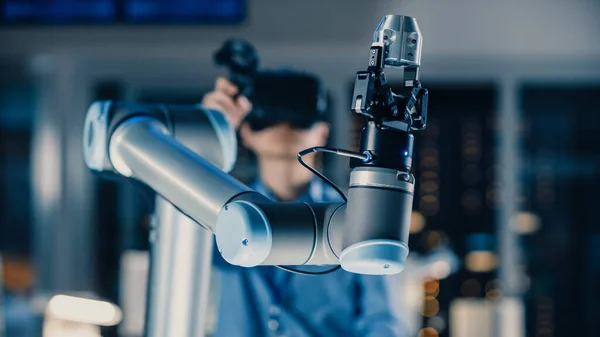Közelkép egy futurisztikus robotkarról, melyet egy profi fejlesztő mérnök irányít virtuális valóság headset-tel és Joysticksszel egy csúcstechnológiás kutató laboratóriumban modern berendezésekkel — Stock Fotó