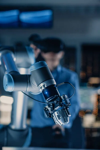 Primer plano vertical de un brazo robótico futurista controlado por un ingeniero de desarrollo profesional con auriculares de realidad virtual y joysticks en un laboratorio de investigación de alta tecnología con equipos modernos —  Fotos de Stock