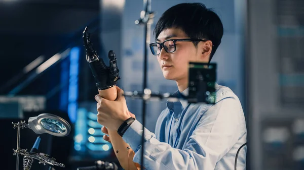 Futuristic Prosmentistic Robot Arm Being Tested by an Professional Japanese Development Engineer in a High Tech Research Laboratory with Modern Computer Equipment. → 현대 컴퓨터 장비를 갖춘 일본의 전문 개발 엔지니어에 의해 시험받고 있다. 그는 그 결과에 만족하고 있다. — 스톡 사진