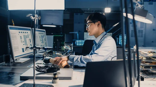 Futuristische prothetische robot arm wordt getest door een professionele Japanse Development Engineer in een High Tech Research Laboratorium met moderne computerapparatuur. Hij is tevreden met het resultaat.. — Stockfoto