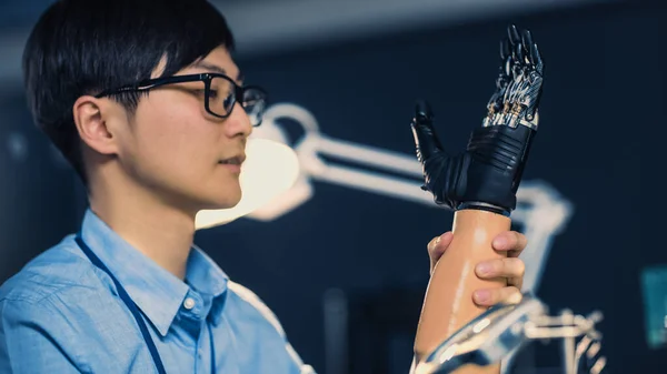 Κοντινό πλάνο ενός φουτουριστικού προσθετικού βραχίονα ρομπότ που δοκιμάζεται από έναν επαγγελματία Ιάπωνα μηχανικό ανάπτυξης σε ένα εργαστήριο έρευνας υψηλής τεχνολογίας με σύγχρονο εξοπλισμό υπολογιστών. — Φωτογραφία Αρχείου