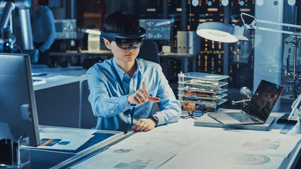 Ingegnere giapponese di sviluppo professionale sta lavorando in un auricolare AR, facendo gesti di toccare pezzi grafici virtuali nel laboratorio di ricerca high-tech con moderne attrezzature informatiche. — Foto Stock
