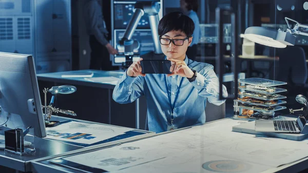 Engenheiro de desenvolvimento japonês profissional em camisa azul está olhando para a realidade aumentada de desenhos técnicos em seu Smartpgone no laboratório de pesquisa de alta tecnologia com equipamento de computador moderno. — Fotografia de Stock