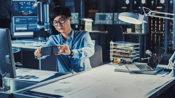 Handsome Japanese Development Engineer in Blue Shirt is looking at Augmented Realirty From Technical Drawings on His Smartpgone in the High Tech Research Laboratory with Modern Computer Equipment. — Stock fotografie