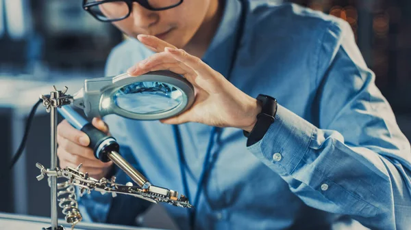 Primo piano di un ingegnere di sviluppo giapponese professionista in camicia blu Saldatura di un circuito stampato in un laboratorio di ricerca high-tech con moderne attrezzature informatiche. — Foto Stock