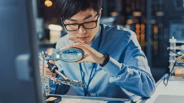 Nahaufnahme eines professionellen japanischen Elektronikentwicklungsingenieurs in blauem Hemd beim Löten einer Leiterplatte in einem High-Tech-Forschungslabor mit moderner Computerausrüstung. — Stockfoto