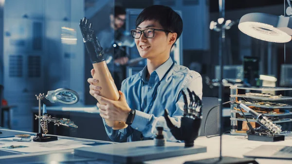 Futuristic Prosmentistic Robot Arm Being Tested by an Professional Japanese Development Engineer in a High Tech Research Laboratory with Modern Computer Equipment. → 현대 컴퓨터 장비를 갖춘 일본의 전문 개발 엔지니어에 의해 시험받고 있다. 그는 그 결과에 만족하고 있다. — 스톡 사진