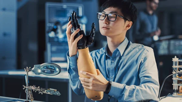 Brazo robótico protésico futurista probado por un ingeniero de desarrollo japonés profesional en un laboratorio de investigación de alta tecnología con equipos informáticos modernos. Él está satatificado con el resultado. —  Fotos de Stock