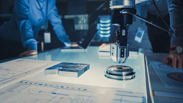 Primer plano de un brazo robótico futurista que recoge un objeto metálico y lo mueve. Equipo de ingenieros siguiendo este proceso avanzado. Están en un laboratorio de investigación de alta tecnología con equipos modernos. — Foto de Stock