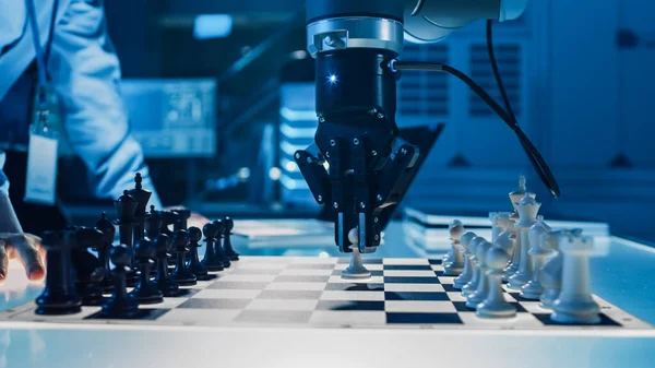 Gros plan sur une intelligence artificielle utilisant un bras robotique futuriste dans un jeu d'échecs contre un humain. Robot déplace un pion. Ils sont dans un laboratoire de recherche moderne de haute technologie. — Photo
