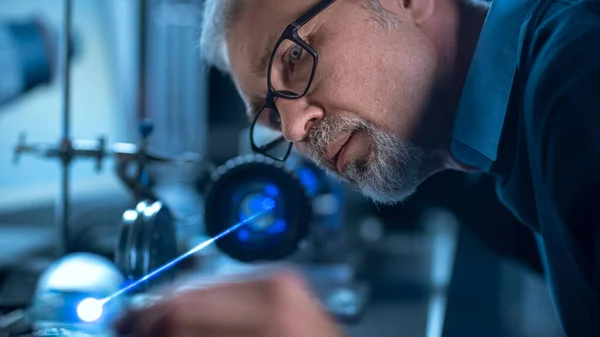 Retrato de primer plano del ingeniero de mediana edad enfocado en gafas que trabaja con equipos láser de alta precisión, utilizando lentes y probando la óptica para obtener precisión Electrónica requerida — Foto de Stock