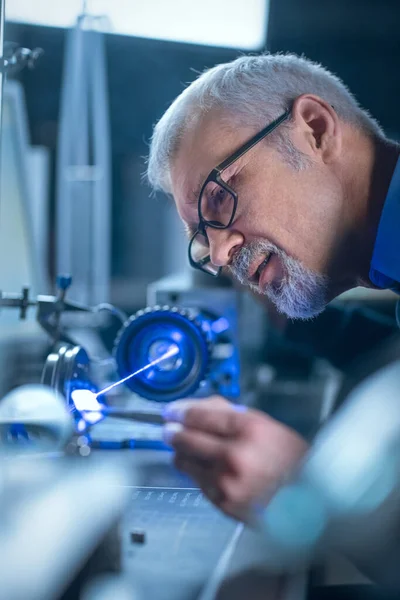 Portret z bliska Skupionego Inżyniera w Okularach pracującego z precyzyjnym urządzeniem laserowym, wykorzystującym soczewki i optykę testową dla dokładności Wymagana elektronika — Zdjęcie stockowe