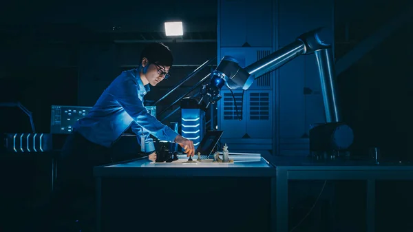Japanese Development Engineer is Testing an Artificial Intelligence Interface by Playing Chess with a Futuristic Robotic Arm. They are in a High Tech Modern Research Laboratory with Low Key Light.