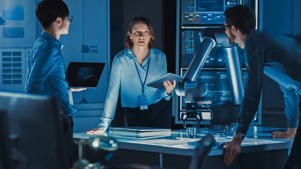 Diverse Team of Engineers with Laptop and a Tablet Analyse and Discuss How a Futuristic Robotic Arm Works and Moves a Metal Object. Nacházejí se v High Tech Research Laboratory s moderním zařízením. — Stock fotografie