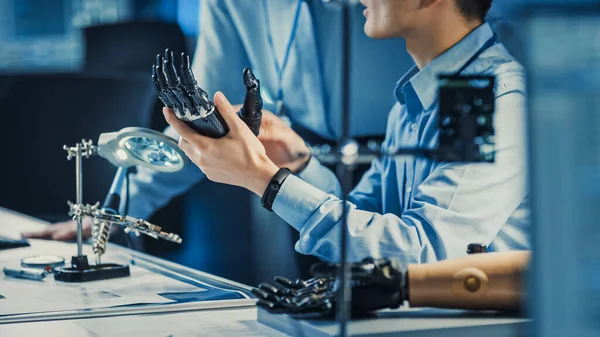 Braço de robô protético tecnológico é testado por dois engenheiros de desenvolvimento profissional em um laboratório de pesquisa de alta tecnologia com equipamentos futuristas modernos. Homem e Mulher Comparar Dados em um Pessoal — Fotografia de Stock