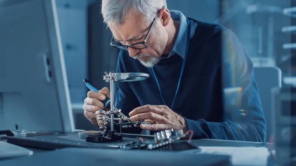 Electronics Maintenance Engineer Soldering Motherboard, Microchip and Circuit Board, Looking through Magnifying Glass, Consults Personal Computer. Ремонт і випробування електроніки — стокове фото